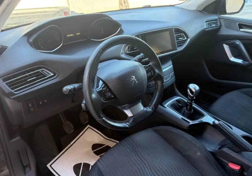 Vue intérieure de la Peugeot 308 Active 2014 noire, montrant le volant, tableau de bord et levier de vitesse manuel.