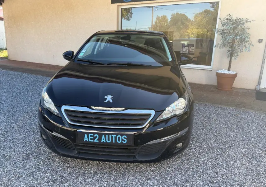 Peugeot 308 Active noire vue de face, avec calandre chromée et plaque AE2 AUTOS visible.