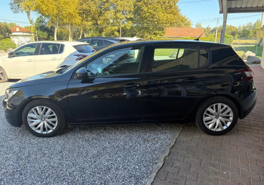 Peugeot 308 Active noire vue de profil côté gauche, garée sur sol mixte gravier et pavés sous abri.