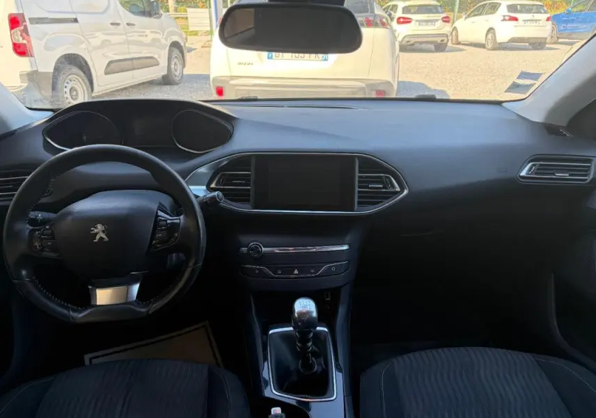 Intérieur noir de Peugeot 308 Active 2014, vue frontale du tableau de bord avec volant et levier de vitesses manuel.
