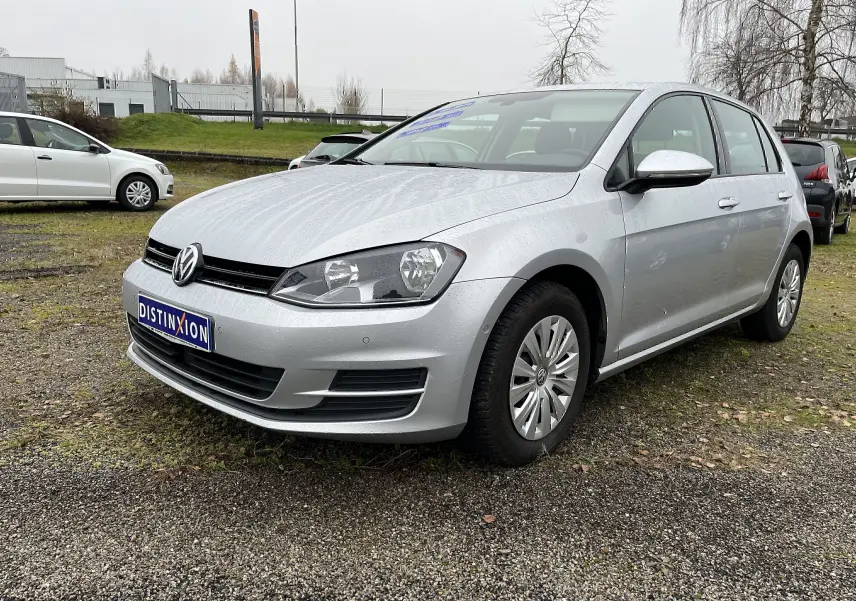 Volkswagen Golf 7 argent vue 3/4 avant droit sur parking avec carrosserie mouillée par la pluie.