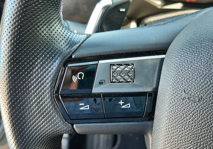Gros plan sur les commandes du volant en cuir perforé du DS3 Crossback gris foncé, avec boutons de volume et commande vocale.
