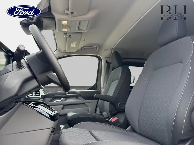 Vue intérieure côté conducteur du Ford Transit Custom Fourgon 2026, sièges gris avec accoudoir et tableau de bord moderne.