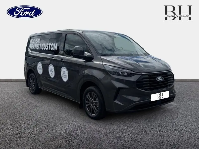 Vue 3/4 avant droit du Ford Transit Custom Fourgon gris Magnetic métallisé avec marquages publicitaires sur la porte latérale.