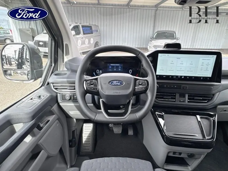 Vue intérieure avant du Ford Transit Custom Fourgon 2026, tableau de bord gris avec écran tactile et volant multifonctions.