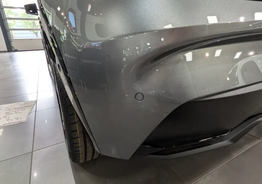 Gros plan sur l'angle avant droit gris schiste d'une Renault Clio VI TCe 115 CH TECHNO, avec capteur de stationnement visible.