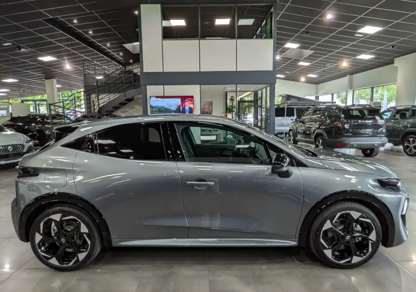 Profil droit d'une Renault Clio VI TCe 115 CH TECHNO gris schiste avec jantes bi-ton et vitres teintées en showroom.
