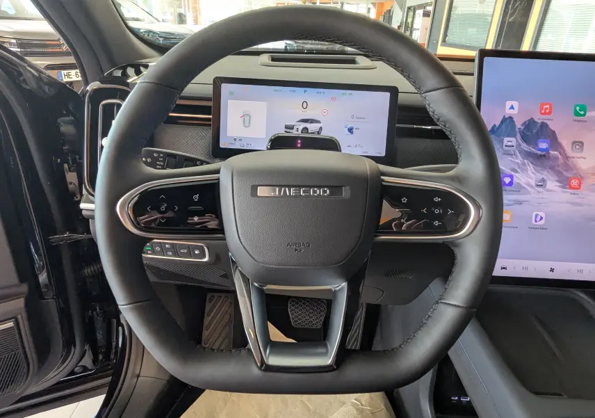 Vue rapprochée du volant noir cuir du JAECOO J7 1.5 TGDI PHEV 205CH EXCLUSIVE avec tableau de bord numérique et écran tactile.
