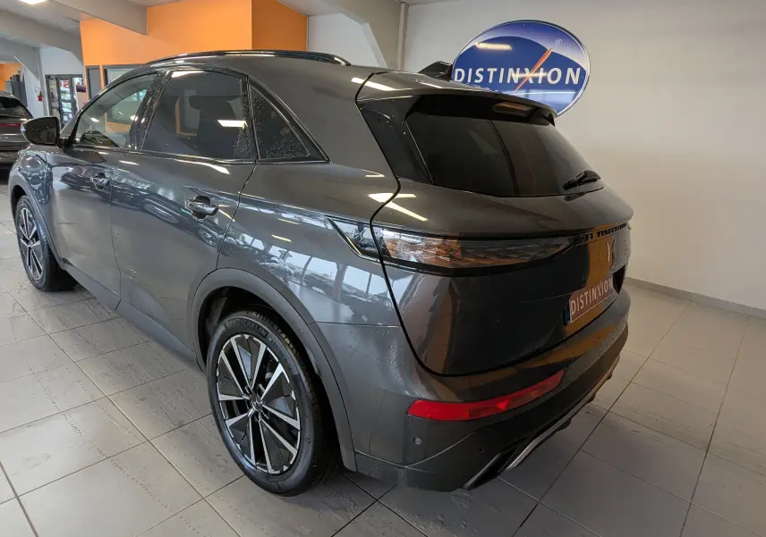 Vue 3/4 arrière droite du DS7 gris laqué avec jantes alliage 19 pouces et vitres teintées en intérieur showroom.
