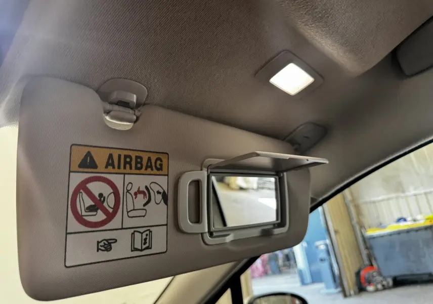 Vue intérieure côté conducteur sur le pare-soleil gris clair avec miroir et avertissement airbag éclairé.