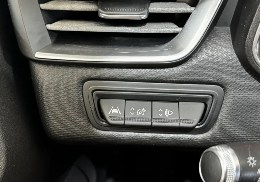 Gros plan sur les boutons de réglage des aides à la conduite et des phares dans une Renault Clio Business gris clair, côté gauche.