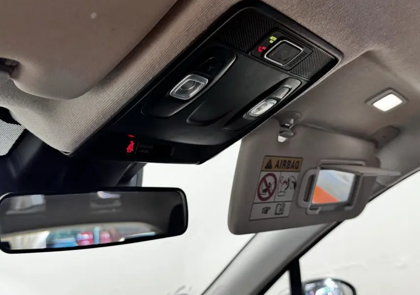 Détail intérieur du plafond avant de la Renault Clio gris clair, avec miroir de soleil ouvert et commandes d’éclairage.