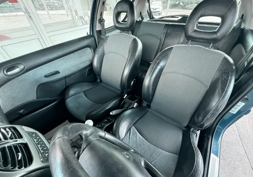 Intérieur de la Peugeot 206 bleu 2003, vue côté conducteur, sièges en cuir et tissu noir, volant cuir visible.