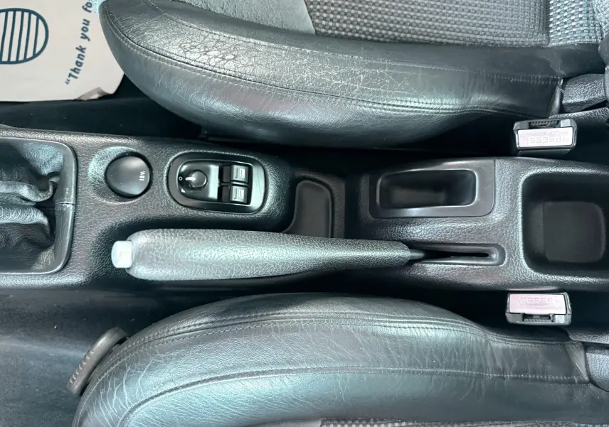 Vue plongeante sur la console centrale noire en cuir et tissu du Peugeot 206 16v 2L avec frein à main et commandes électriques.
