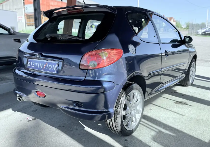 Peugeot 206 bleu en 3/4 arrière droit, avec jantes alliage et aileron de toit visible.