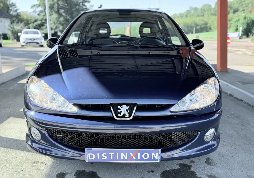 Vue avant d'une Peugeot 206 bleu foncé avec phares allumés et plaque Distinxion visible.
