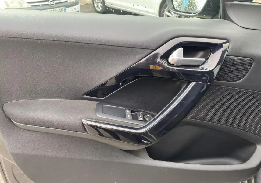 Gros plan sur la porte côté gauche de la Peugeot 208 gris, montrant la poignée et les commandes des vitres électriques.
