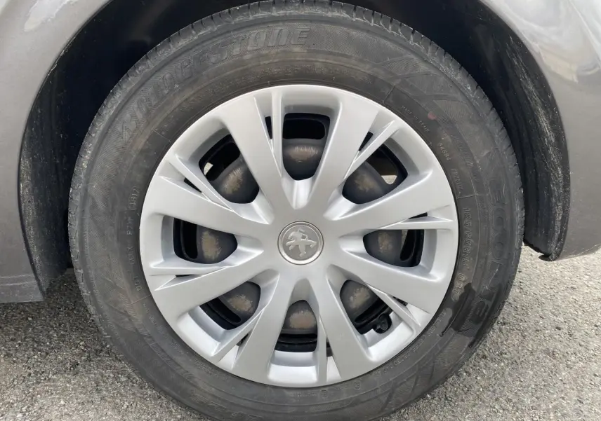 Gros plan sur la roue avant droite grise d'une Peugeot 208 1.2i 12V Active Business avec enjoliveur d'origine.