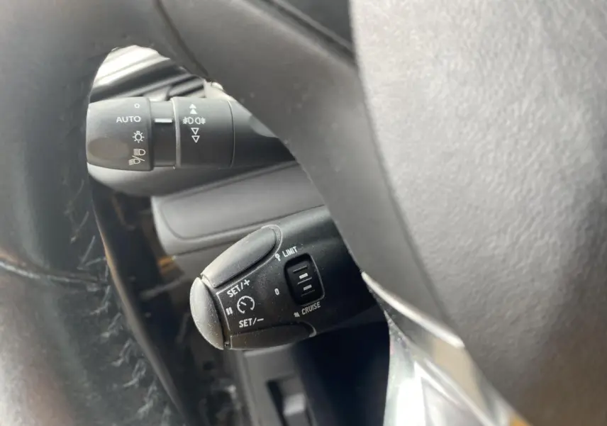 Gros plan sur le volant de la Peugeot 208 gris, montrant la commande du régulateur de vitesse et le commodo d'éclairage.
