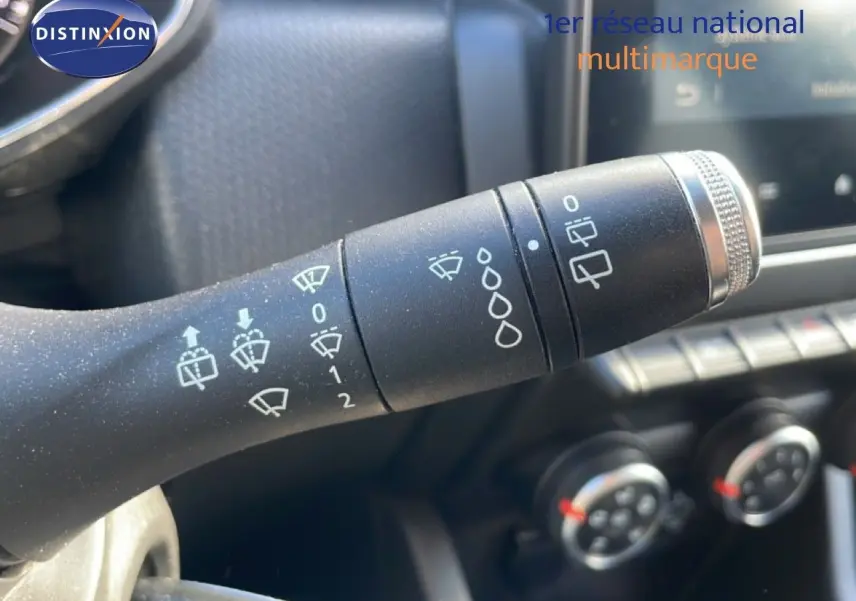 Gros plan sur la manette d'essuie-glace à gauche du volant d'une Renault Clio blanc glacier, tableau de bord en arrière-plan.