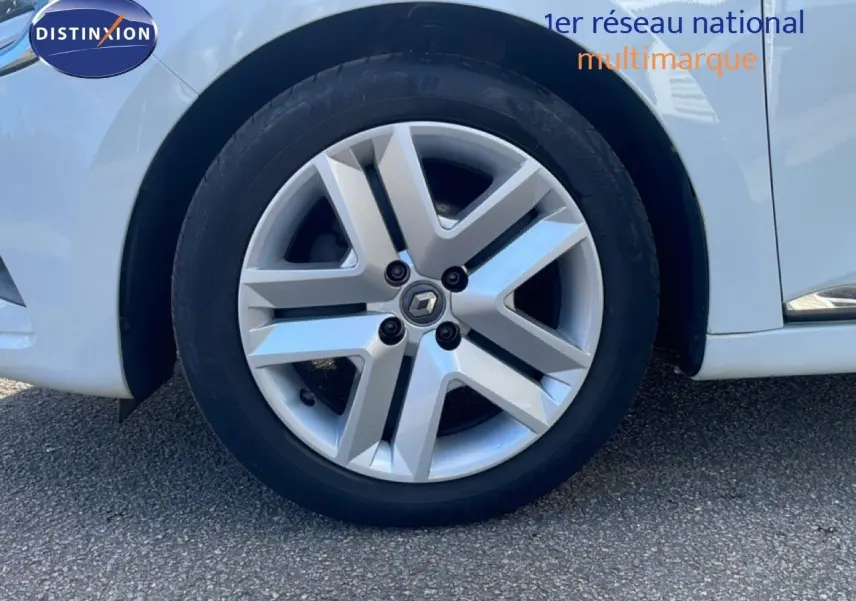 Gros plan sur la roue avant gauche d'une Renault Clio blanc glacier avec jante alliage au design moderne.