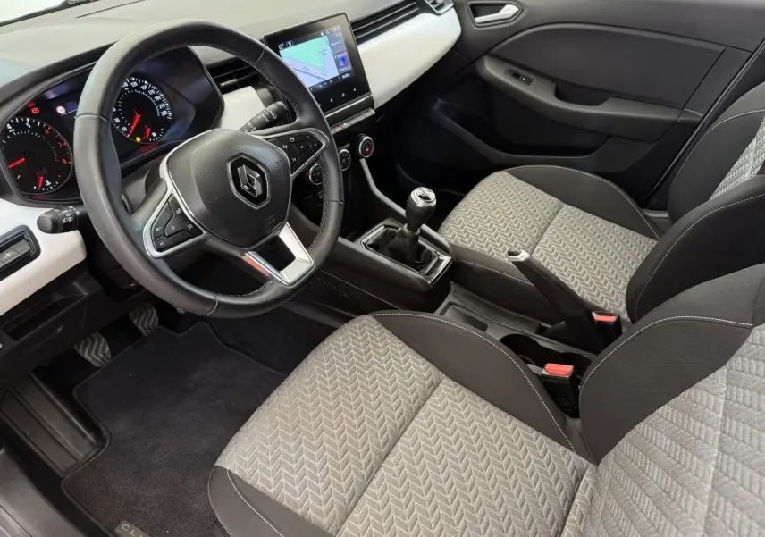 Vue intérieure côté conducteur de la Renault Clio 2023 avec volant cuir, écran tactile central et sièges tissu gris à motifs.