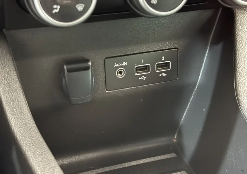 Gros plan sur la console centrale noire de la Renault Clio blanche, montrant les ports USB et prise Aux-IN.