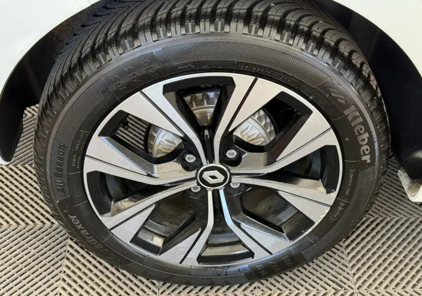 Gros plan sur la roue avant droite d’une Renault Clio blanche, jante alliage bicolore avec logo Renault central.
