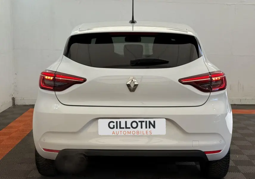 Vue arrière d'une Renault Clio blanche Evolution TCe 100 GPL avec feux LED allumés dans un garage.
