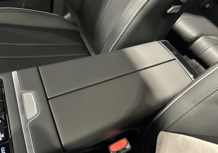 Gros plan sur l'accoudoir central en cuir gris noir du JAECOO J7 TGDI PHEV, avec surpiqûres blanches et bouton de ceinture rouge.