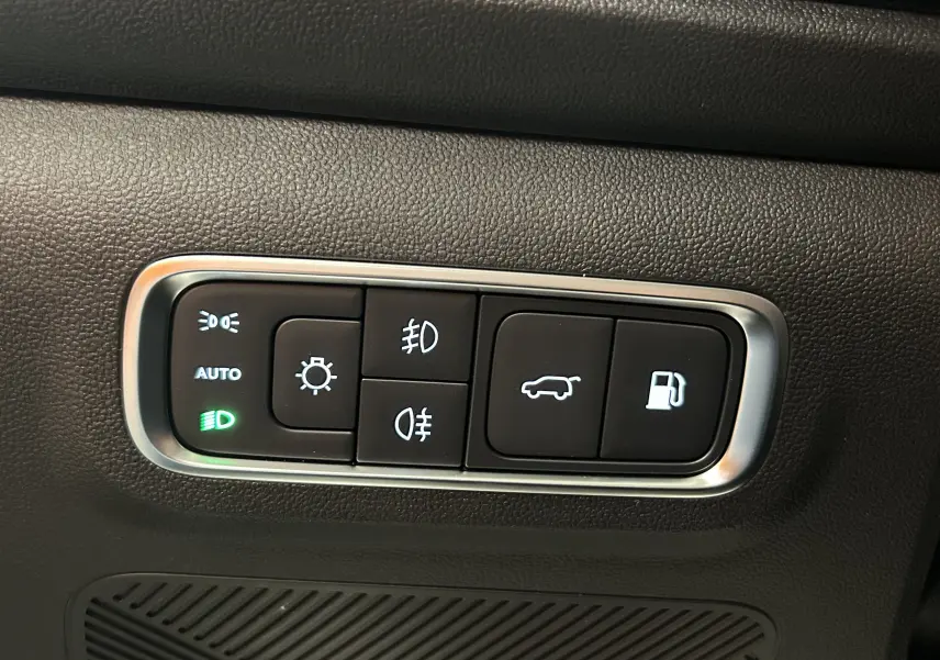 Gros plan sur les commandes d’éclairage et d’ouverture de coffre du JAECOO J7 TGDI PHEV, finition intérieure noire.