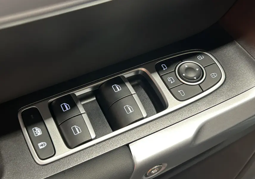 Gros plan sur les commandes de lève-vitres et rétroviseurs du JAECOO J7, finition olive grey metal, côté intérieur porte avant gauche.