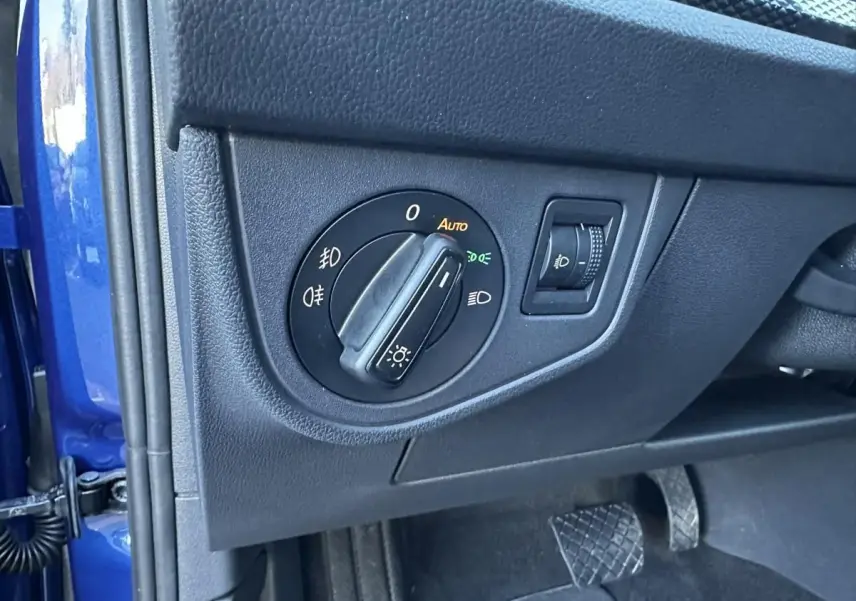 Gros plan sur le bouton de commande des phares à gauche du volant, intérieur noir avec portière bleu Recife visible.