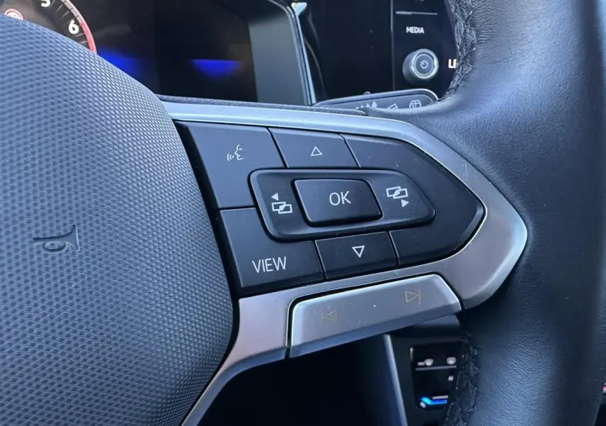 Gros plan sur les commandes multifonctions au volant noir du Volkswagen Taigo Bleu Recife, côté gauche.