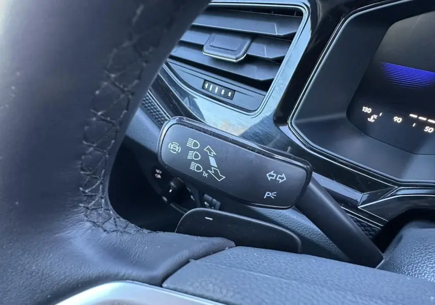 Gros plan sur le commodo gauche du volant en cuir noir du Volkswagen Taigo 2025, avec tableau de bord numérique en arrière-plan.