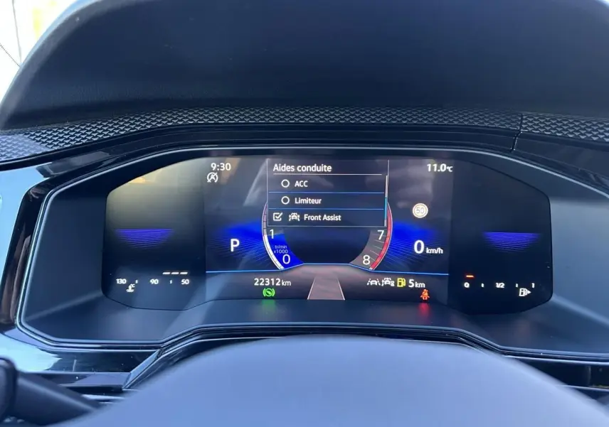 Vue rapprochée du tableau de bord numérique du Volkswagen Taigo bleu Recife, affichant les aides à la conduite et la vitesse à 0 km/h.