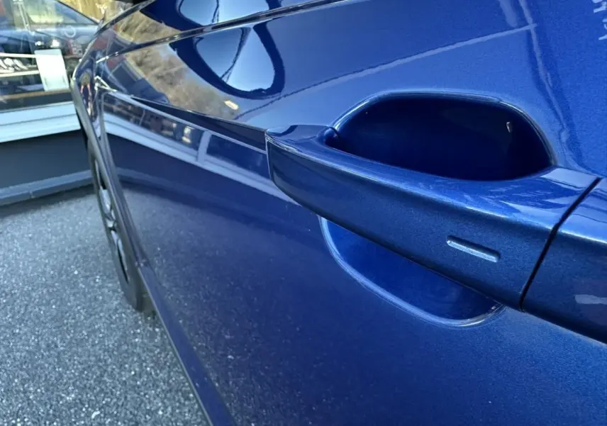 Gros plan sur la poignée de porte côté droit d’un Volkswagen Taigo 2025 bleu Recife avec peinture métallisée.