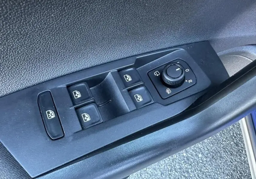 Vue rapprochée des commandes de lève-vitres et réglage des rétroviseurs sur la porte côté conducteur du Volkswagen Taigo bleu Recife.