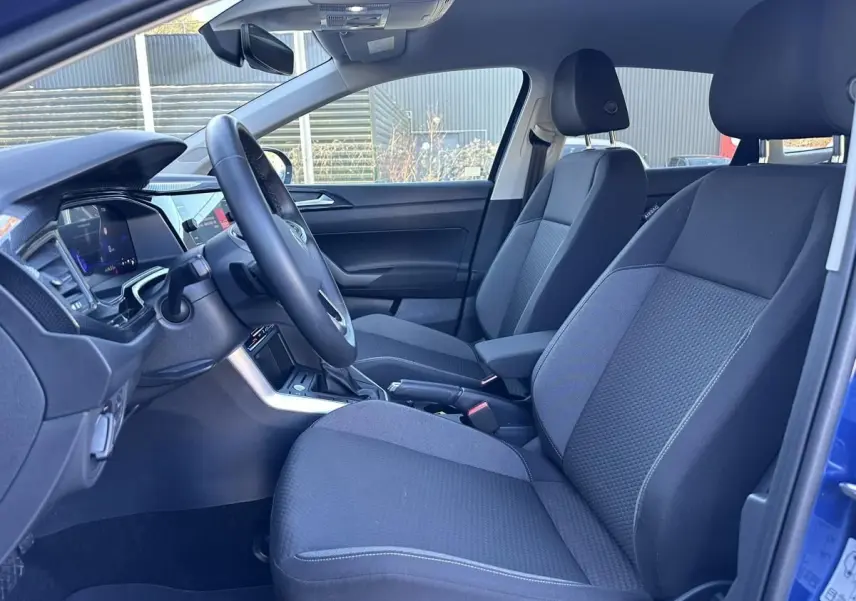 Vue intérieure côté conducteur du Volkswagen Taigo bleu Recife 2025, avec sièges tissu gris et accoudoir central.