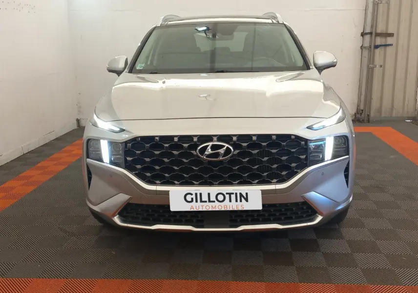 Vue frontale du Hyundai Santa Fe gris clair 2022 avec calandre noire et phares LED allumés dans un garage.