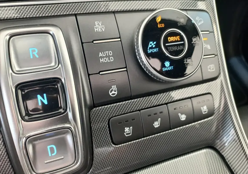 Gros plan sur la console centrale du Hyundai Santa Fe 2022, boutons de boîte auto et sélection modes terrain sur finition carbone.