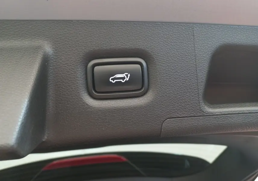 Bouton noir d'ouverture électrique du coffre sur le hayon intérieur d'un Hyundai Santa Fe gris clair.