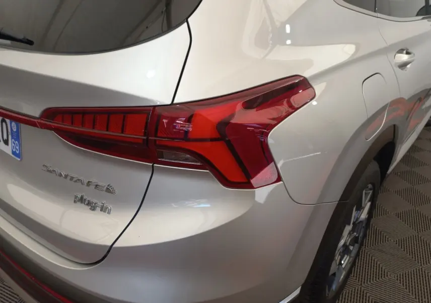 Vue 3/4 arrière droite d’un Hyundai Santa Fe gris clair avec feux arrière LED et badge plug-in visible.