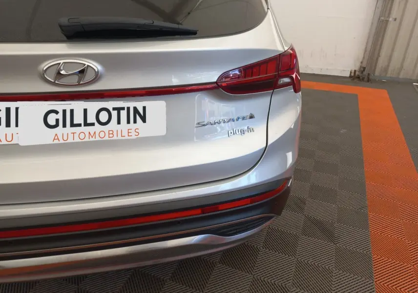 Vue arrière droite du Hyundai Santa Fe gris clair avec logo et badge plug-in visible sur un sol à motifs gris et orange.