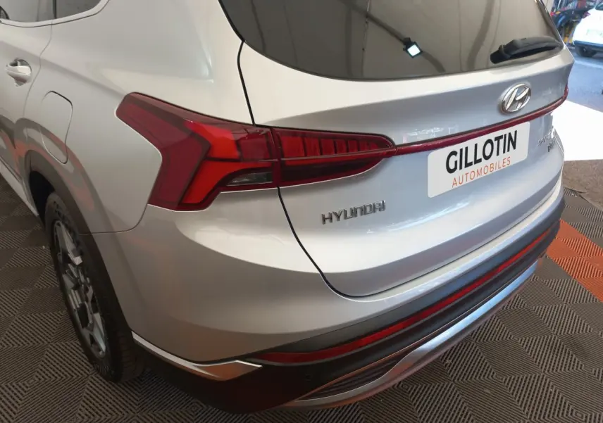 Vue 3/4 arrière droite d’un Hyundai Santa Fe gris clair avec feux arrière LED et logo visible.