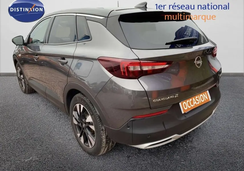 Vue 3/4 arrière droite d'un Opel Grandland X gris Moai métal avec jantes bicolores et feux LED distinctifs.