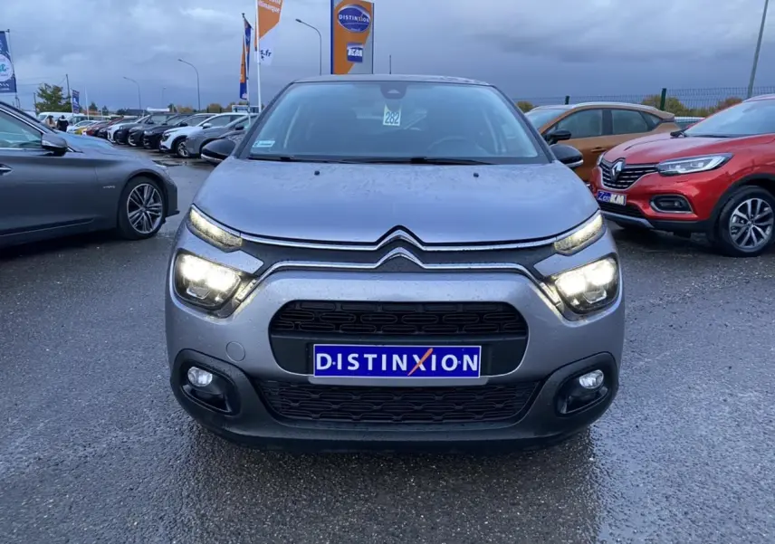 Citroën C3 gris Artense vue de face sous la pluie, feux allumés et calandre noire distinctive.