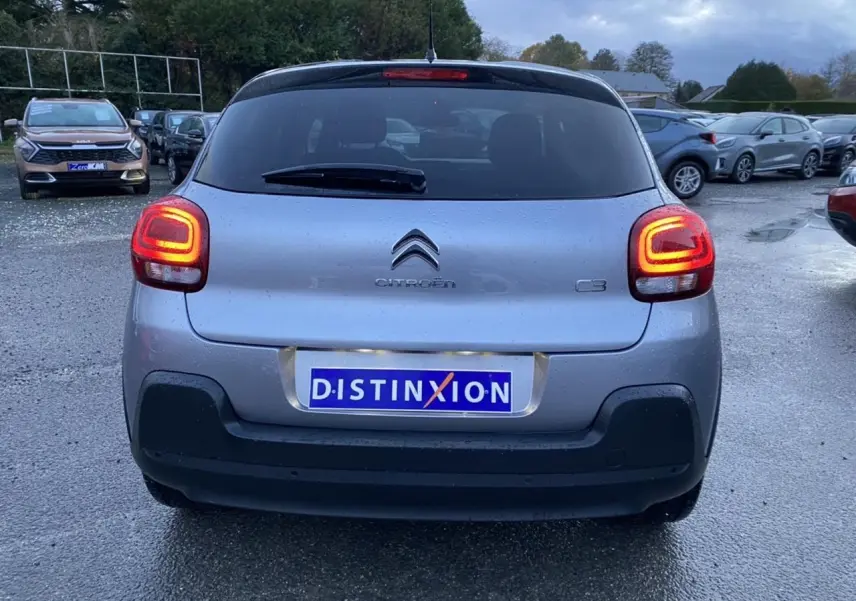 Vue arrière d'une Citroën C3 1.2 essence gris Artense avec feux arrière allumés sur parking humide.