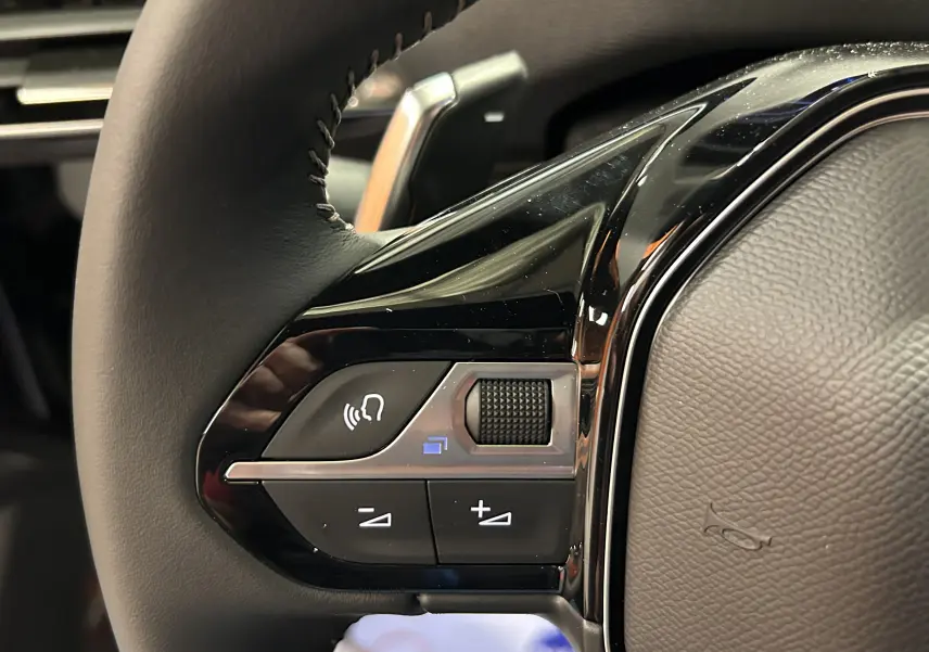 Gros plan sur les commandes du volant noir du Peugeot 5008 2024 finition Allure Pack Gris Platinium.