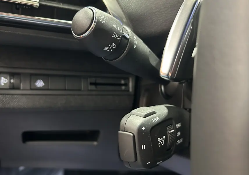 Gros plan sur les commandes au volant du Peugeot 5008 2024, finition Allure Pack, avec régulateur de vitesse et éclairage automatique.